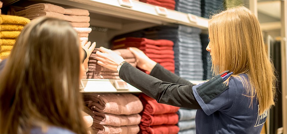 Två butiksarbetare lägger upp nya handdukar på butikshyllan.